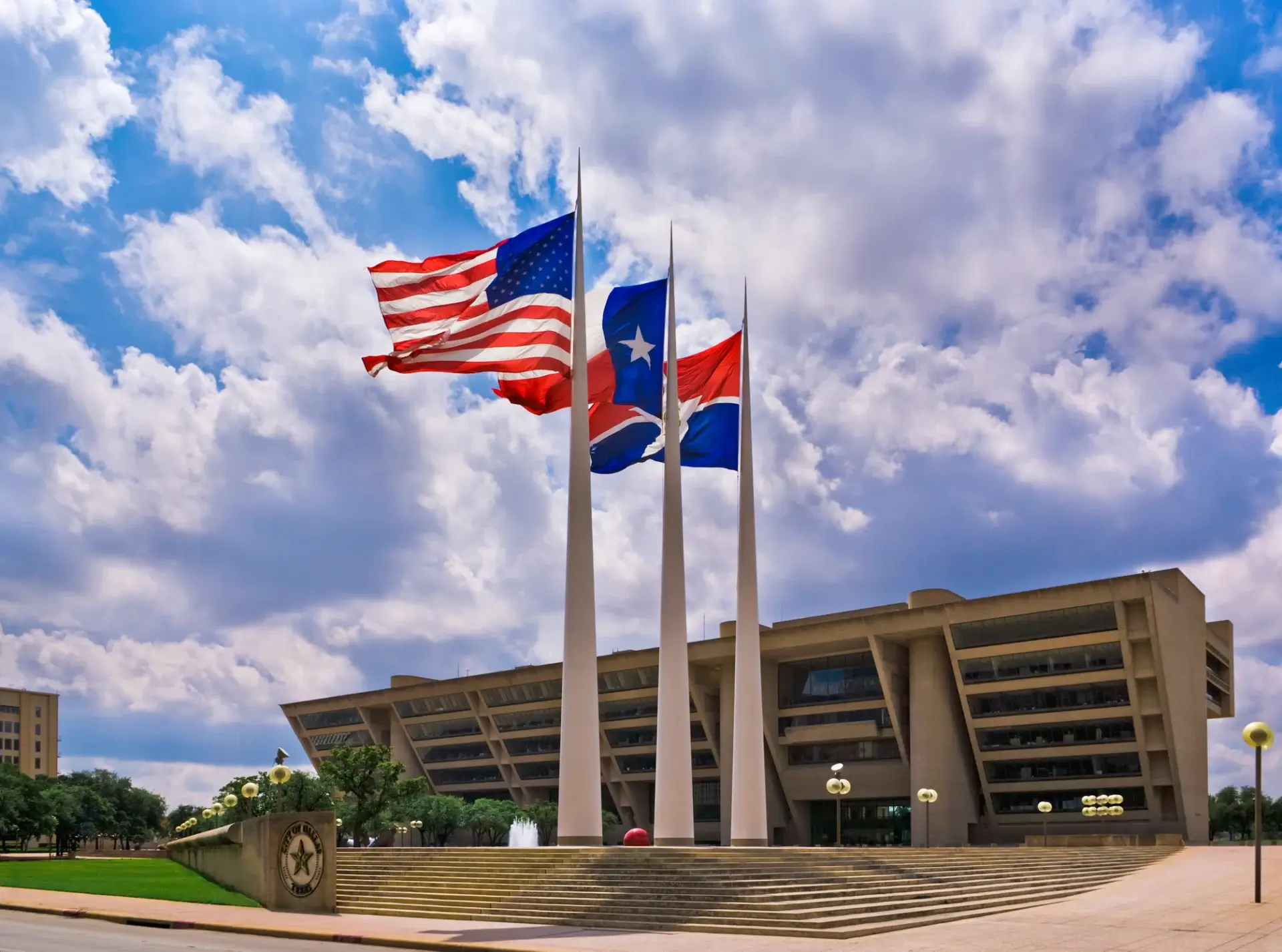 Dallas City Hall with flags under clouds.