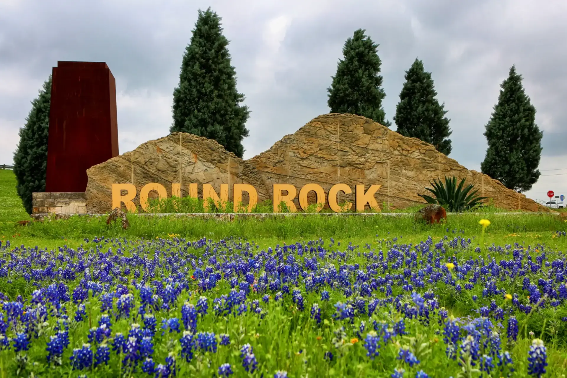 Round Rock sign with bluebonnets and trees.